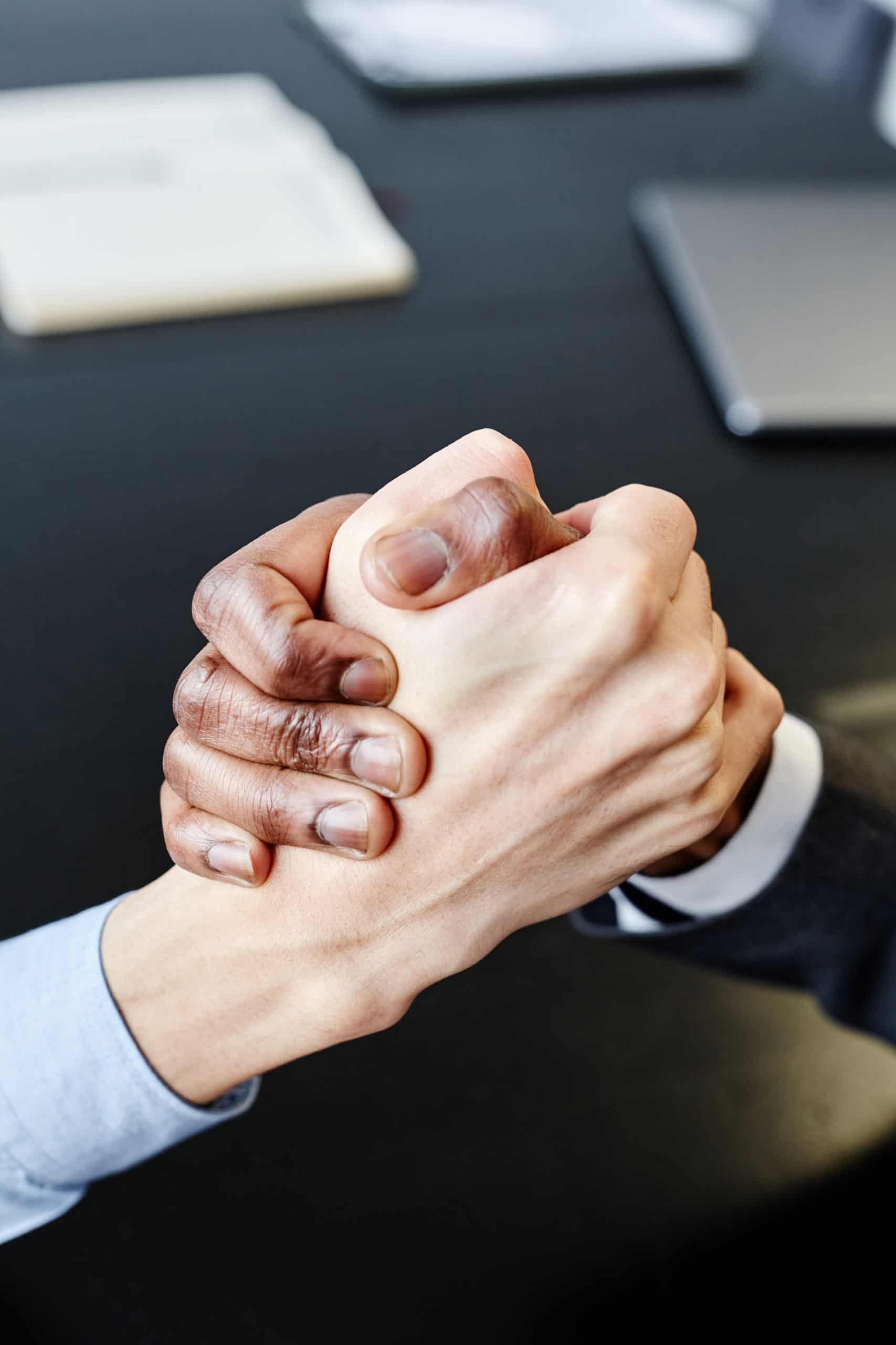 Close up of two business partners shaking hands in unity at meeting table, copy space