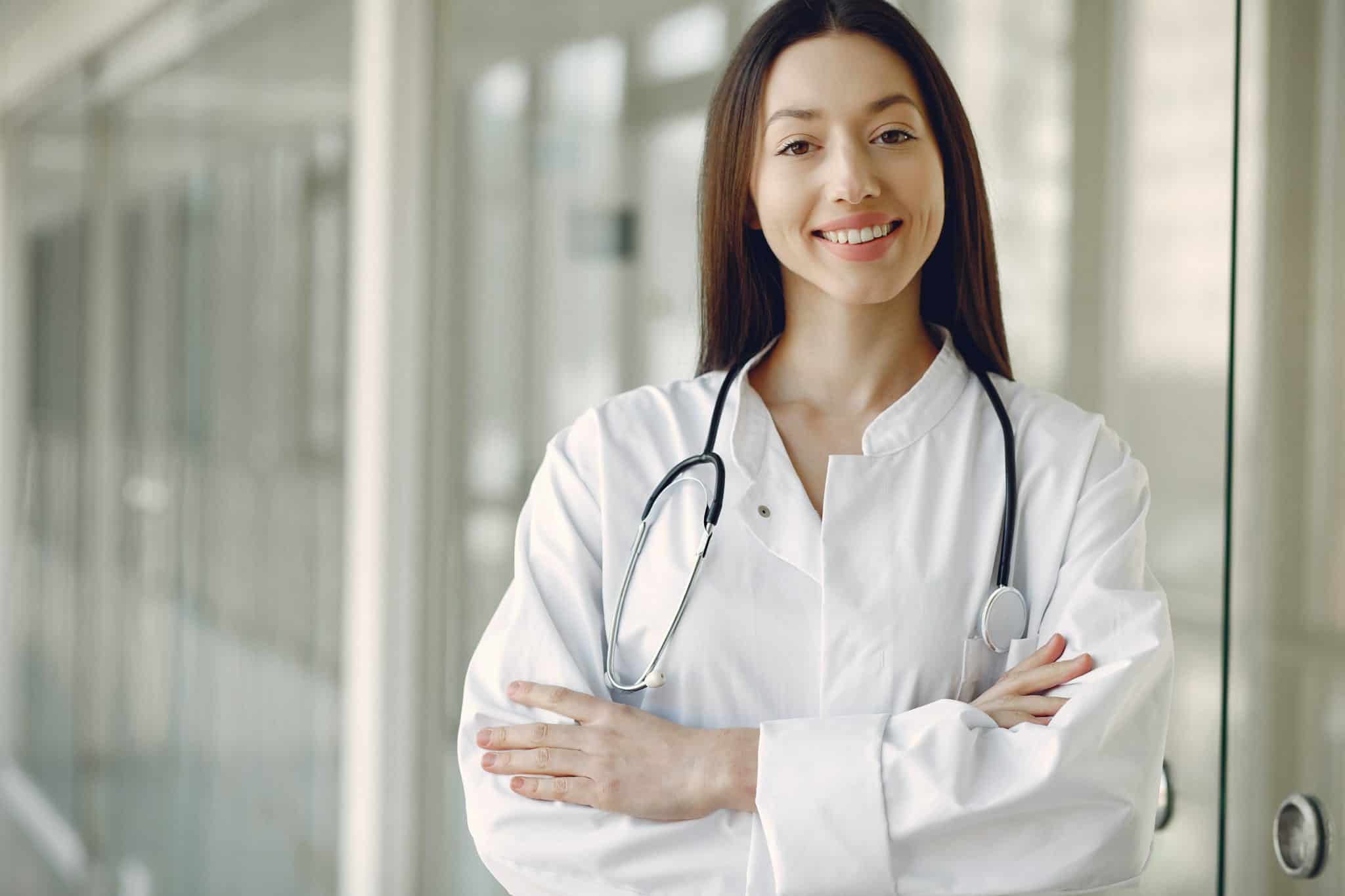 Young doctor smiles as she stands in hallway outside of glass door