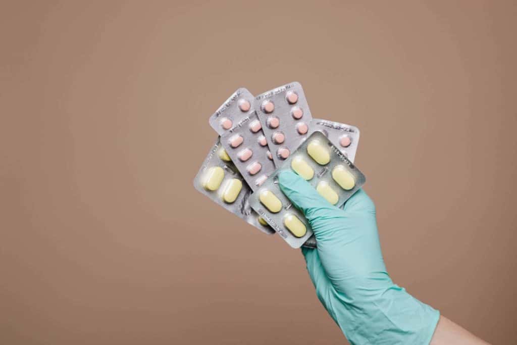 Hand in disposable glove holding 5 packs of different types of medication pills
