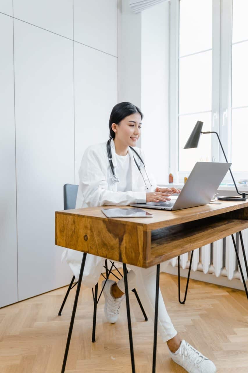 Woman smiling as she sits at a wooden desk doing research on behavioral health services on a laptop